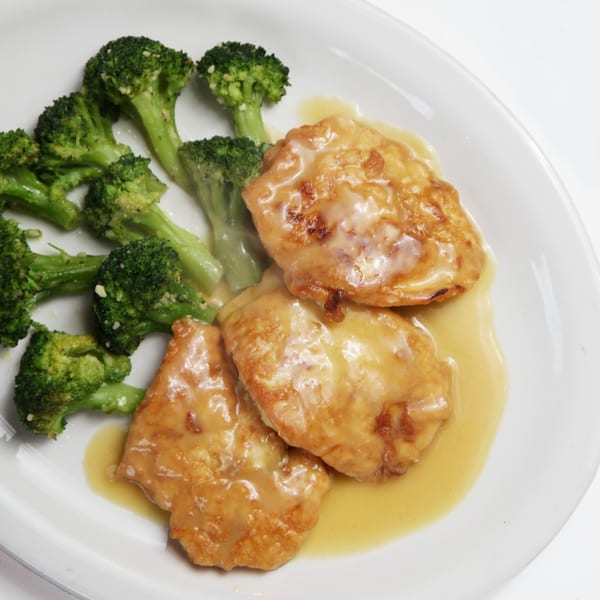 Chicken Francese with a lemon butter sauce and a side of steamed broccoli on a white plate.