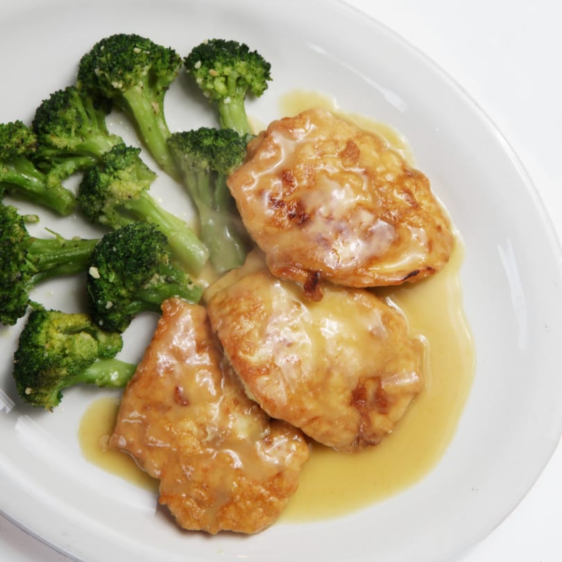Chicken Francese with a lemon butter sauce and a side of steamed broccoli on a white plate.