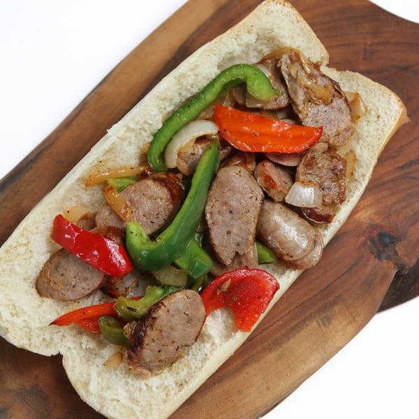 Sausage and peppers hero sandwich on a wooden board, with red and green bell peppers and onions.