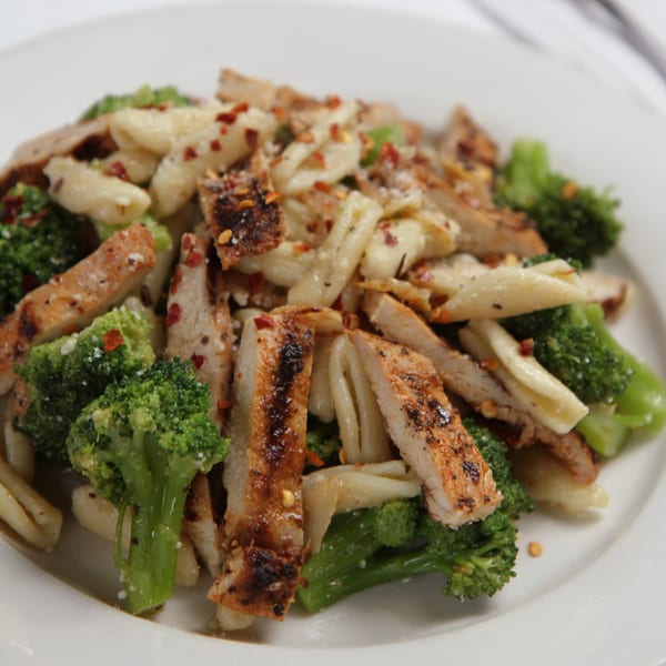 Grilled chicken and broccoli pasta with red pepper flakes on a white plate.