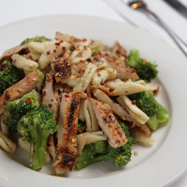 Grilled chicken and broccoli pasta dish, topped with red pepper flakes and grated cheese.