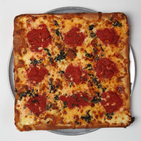 Square Fort Lee Pizzeria pizza with melted cheese, red sauce dollops, and dark green herbs on a metal pan.