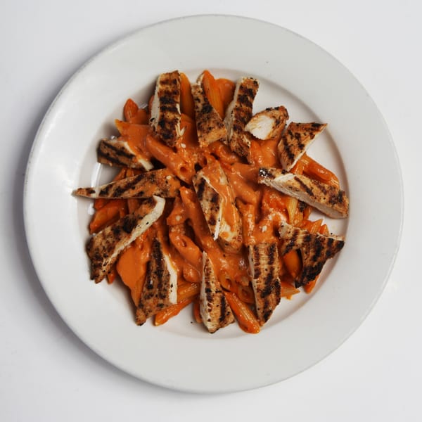 Penne pasta with creamy orange sauce and grilled chicken pieces on a white plate.